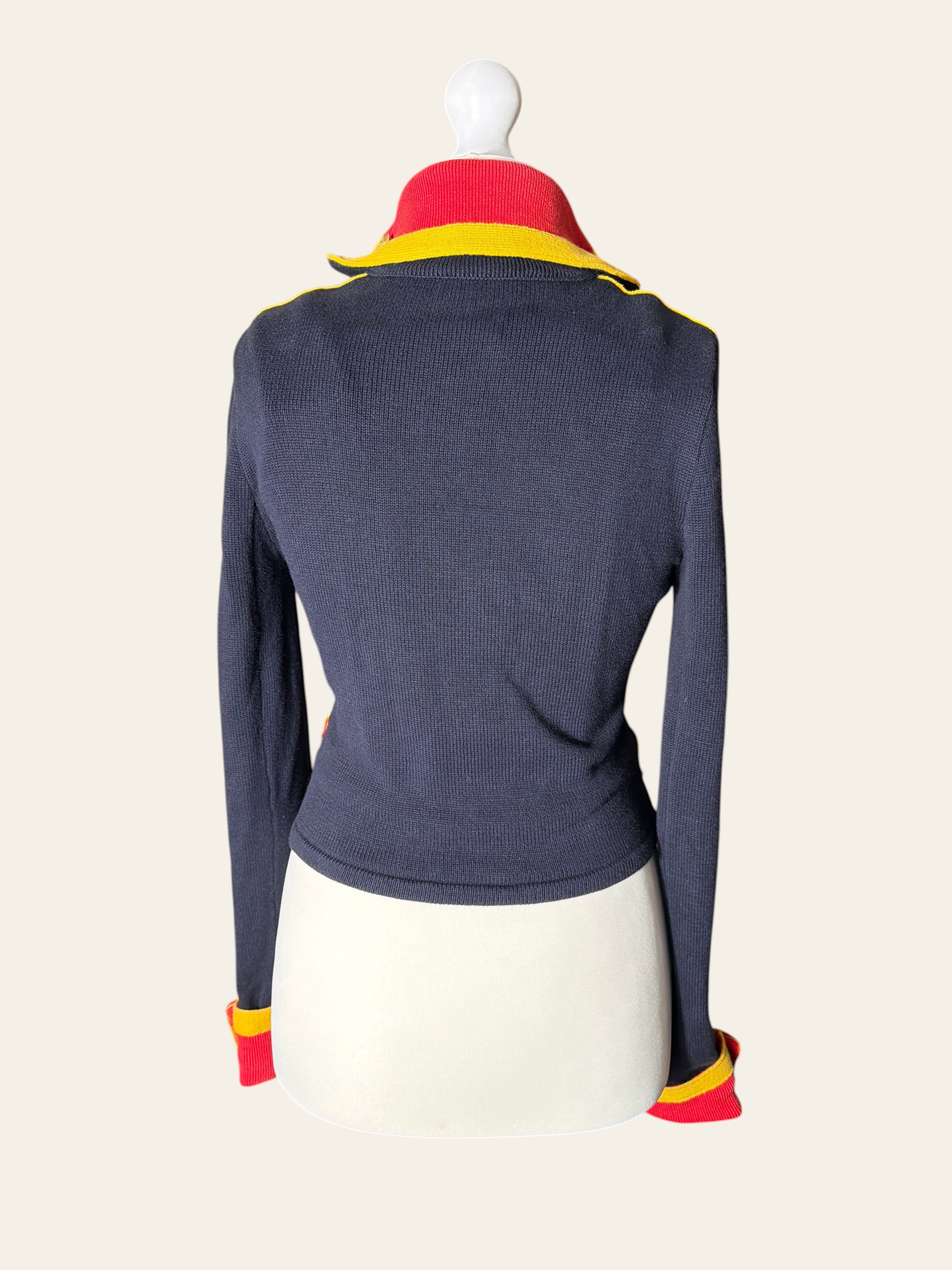 A navy blue ribbed knit long-sleeve top displayed on a mannequin, featuring a red and yellow striped collar and matching red and yellow striped cuffs.