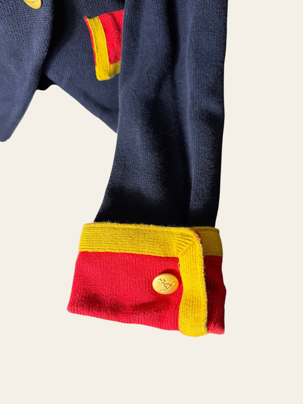 Close-up of a navy knit garment with bright red and yellow cuff details and a matching red and yellow patch, shown against a plain light background.