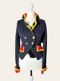 A navy blue cropped double-breasted jacket with yellow and red trim, displayed on a white mannequin torso against a light beige background.