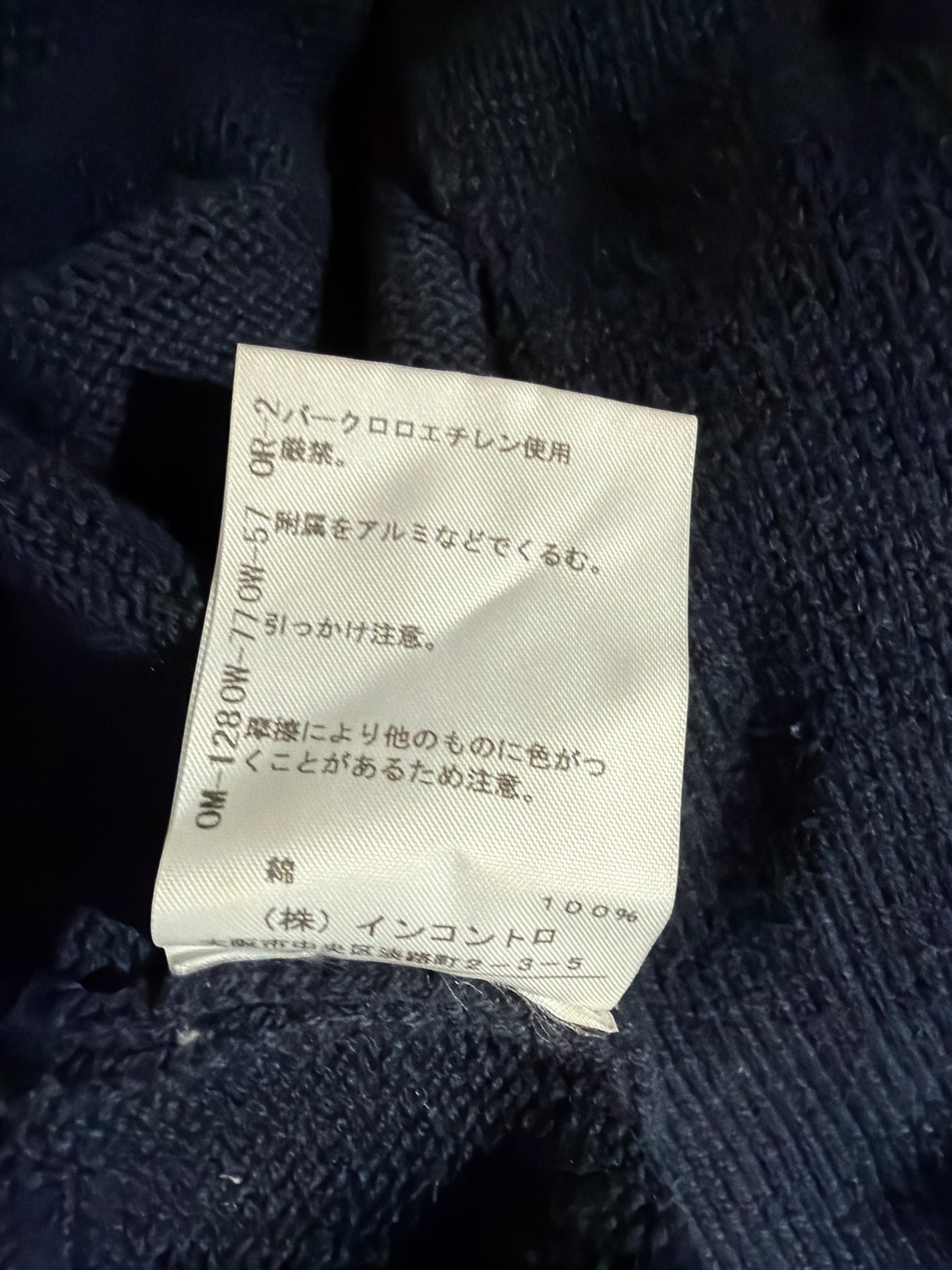 A close-up of a white fabric care label with Japanese text sewn onto dark navy blue knit clothing.