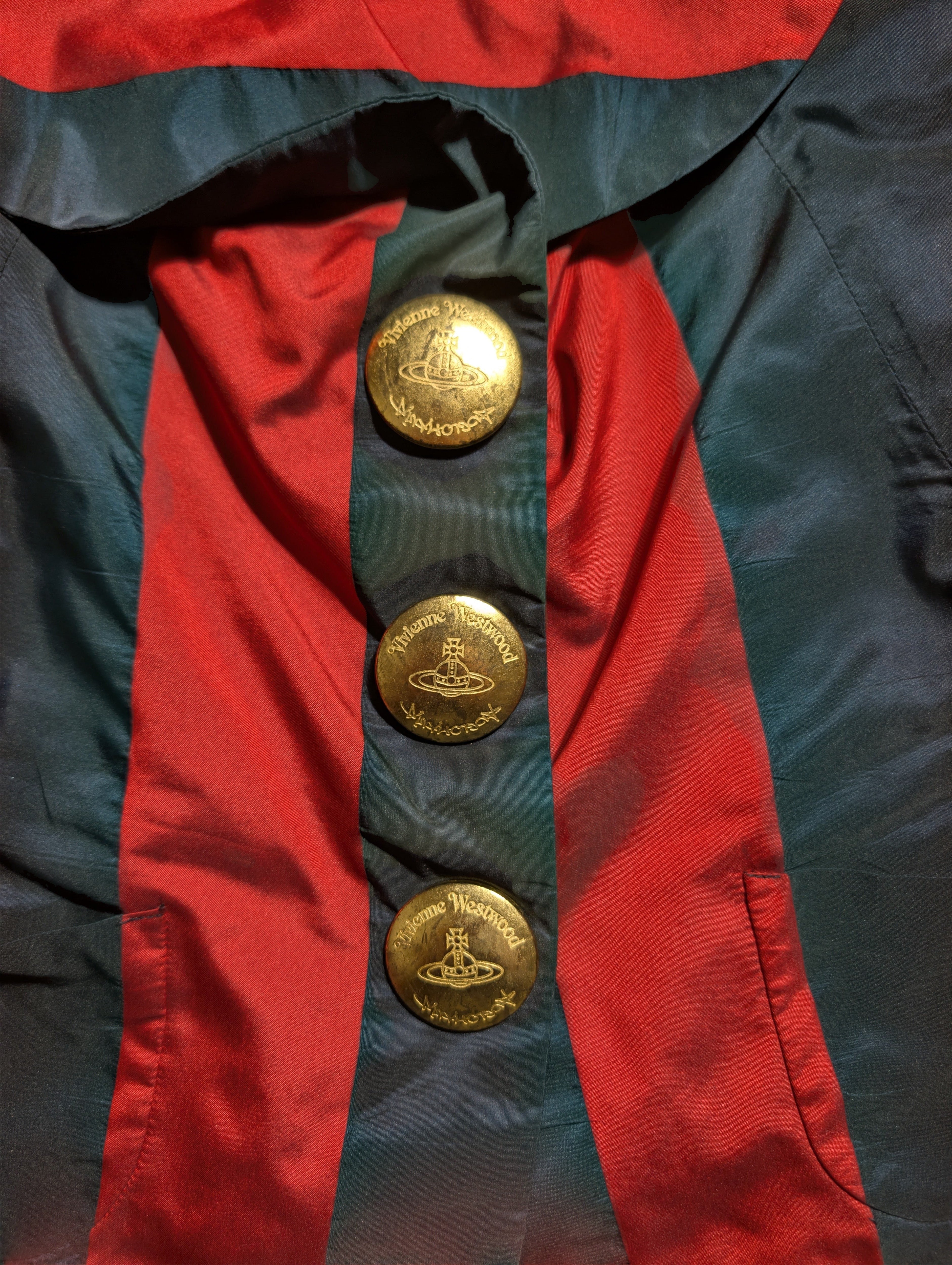 Close-up of a red and dark teal satin-like garment with three large gold buttons featuring the Orb logo, indicating the brand Vivienne Vivienne.