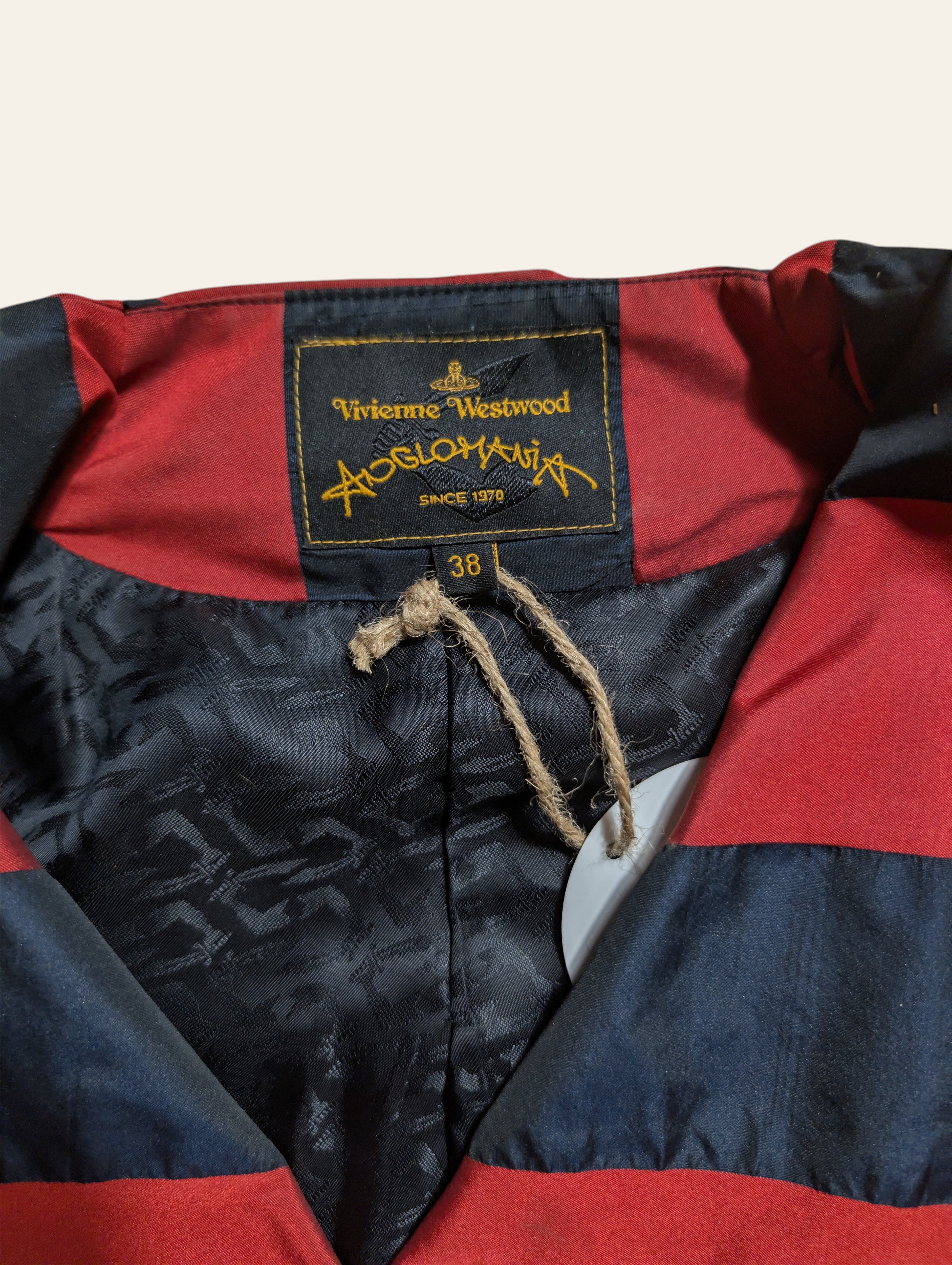 Close-up of a vintage striped jacket with red and navy blue horizontal stripes, featuring a black brand label for 'Viktor's Westwood' with gold embroidery, a twine drawstring, and a paper tag.
