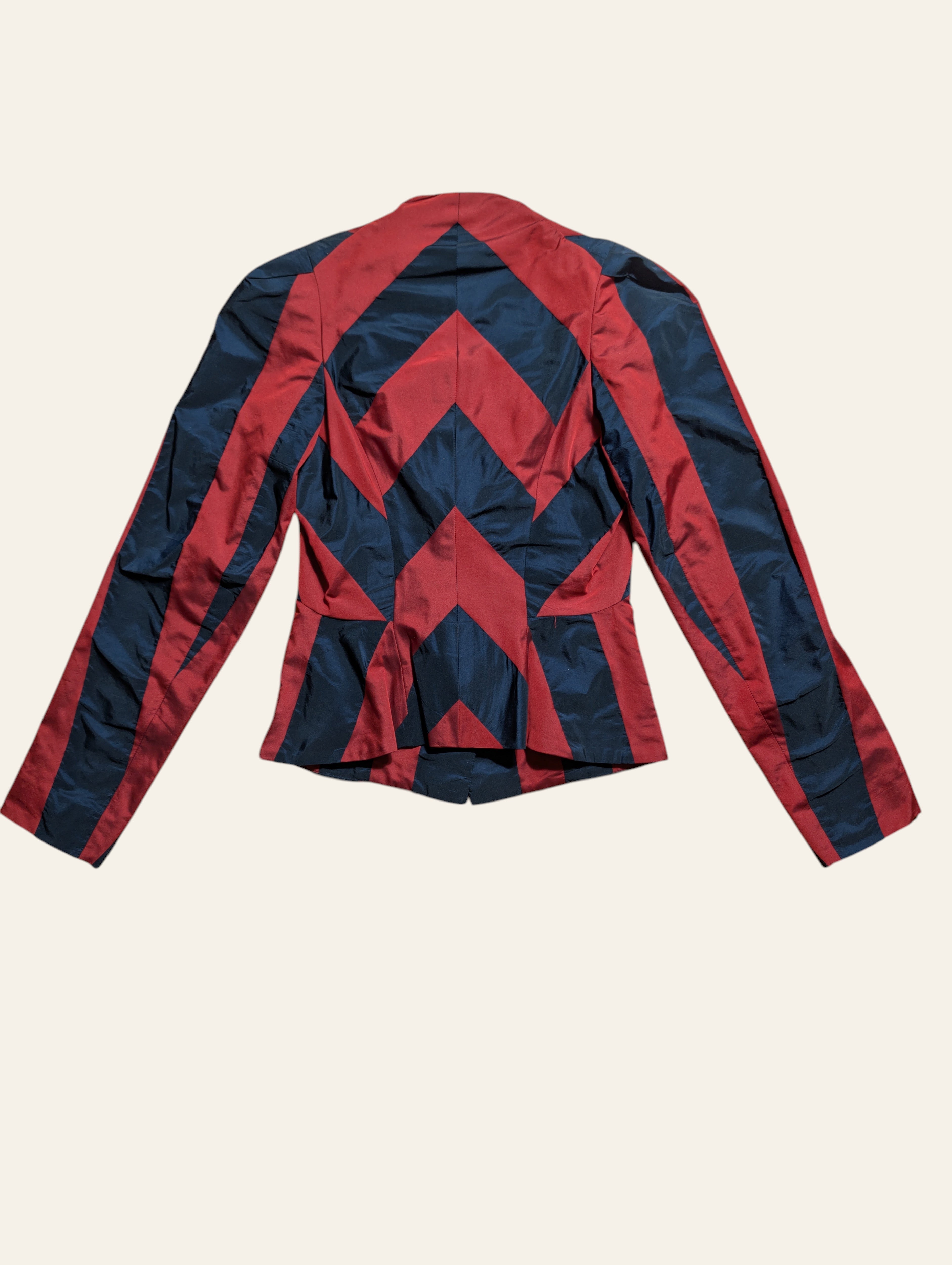 A cropped long-sleeve jacket with a bold geometric chevron pattern in red and navy blue, shown from the back against a light cream background.