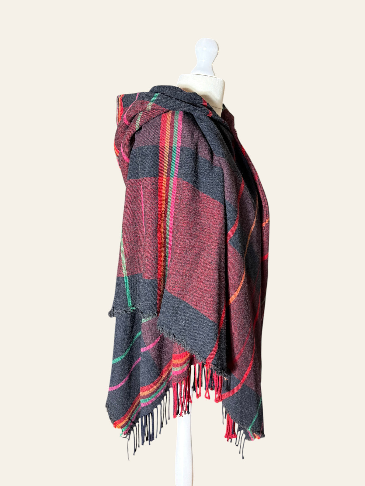 Vivienne Westwood hooded tartan poncho in burgundy, black, and red with fringe hem on a mannequin.